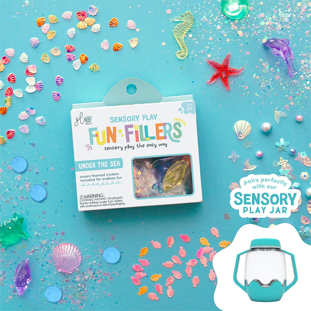 Een demonstratie van glo pals Fun*Fillers 'Under the Sea' sensorisch speelgoed, met de verpakking en diverse kleine, kleurrijke oceaanfiguren en glitters op een blauwe ondergrond, naast een sensorische speelpot.