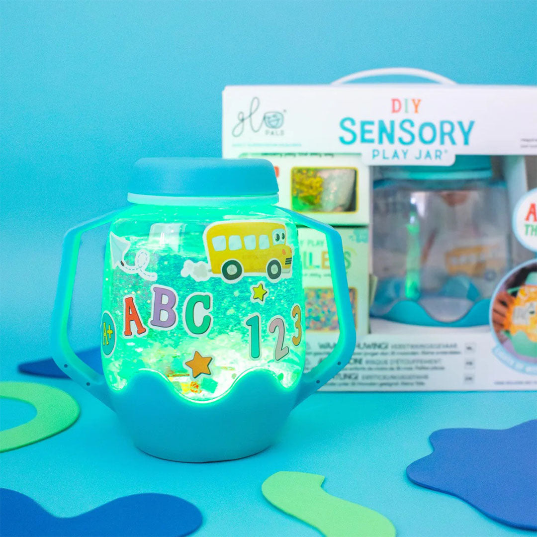 Glo Pals DIY Sensory Play Jar met ABC thema, gevuld met glitter en stickers, gloeit groen op een blauwe achtergrond.