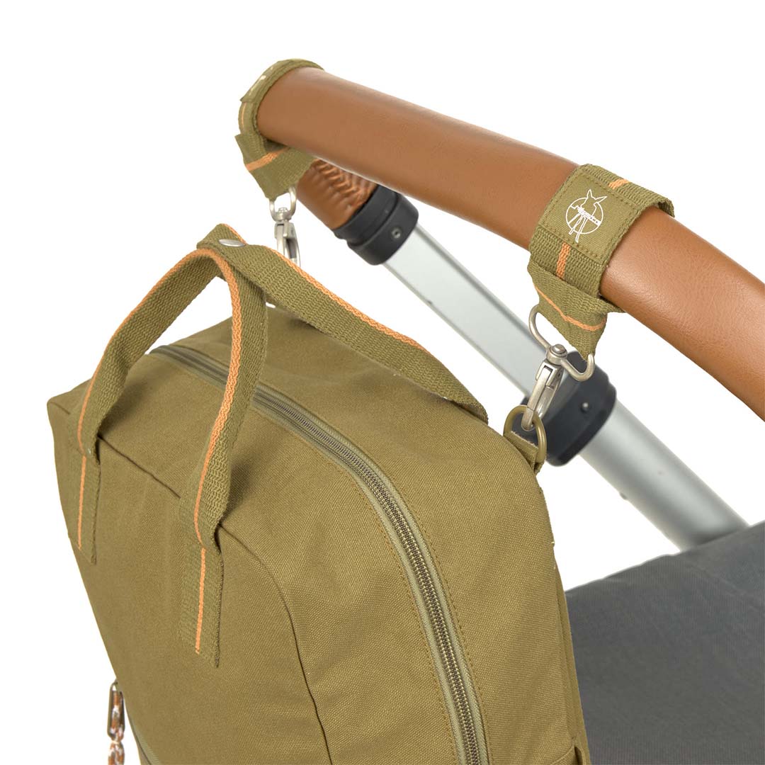 Een olijfgroene accessoiretas hangt met riemen aan de handgreep van een kinderwagen.