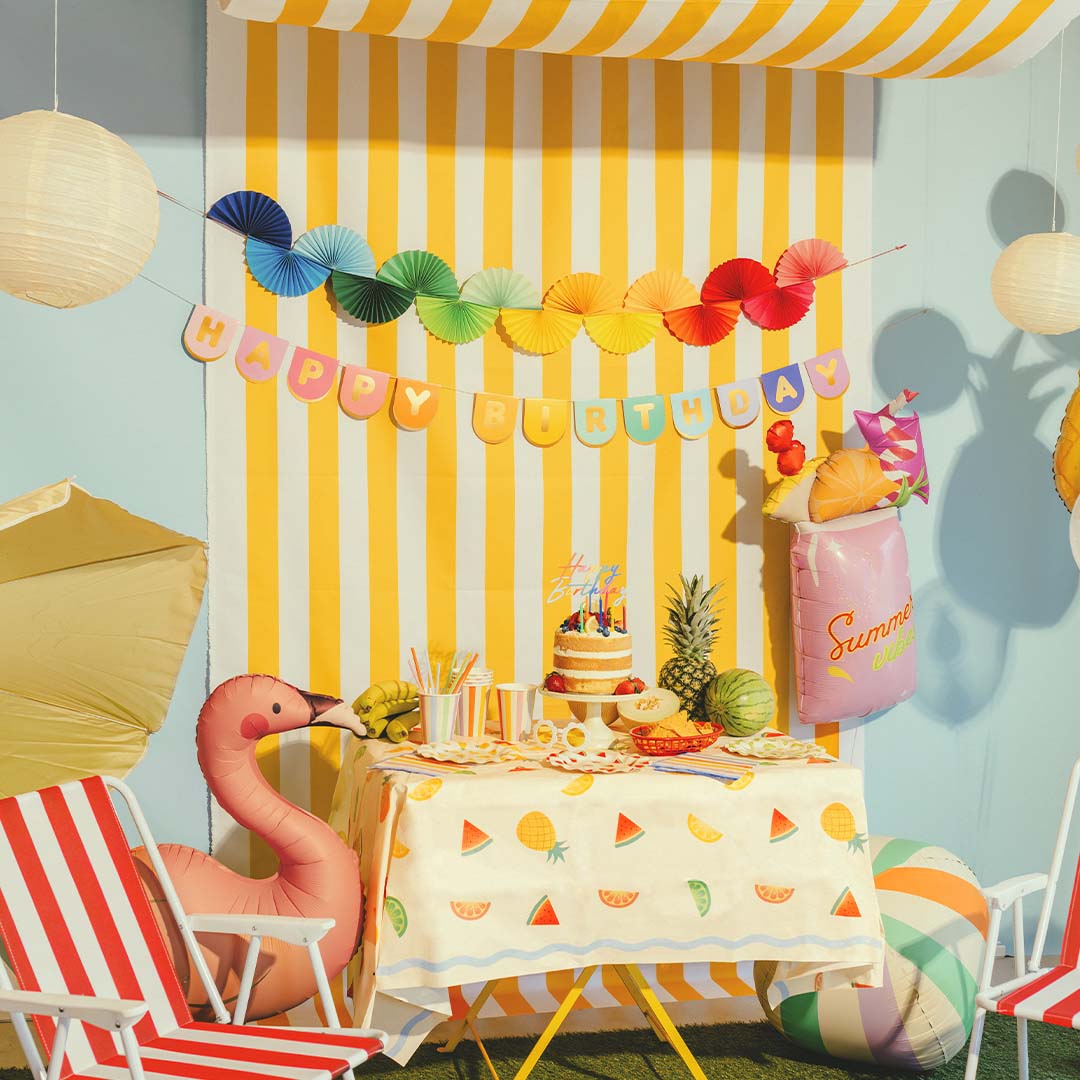 PartyDeco 'Happy Birthday' slinger hangt boven een feesttafel met een taart en zomerse decoraties.