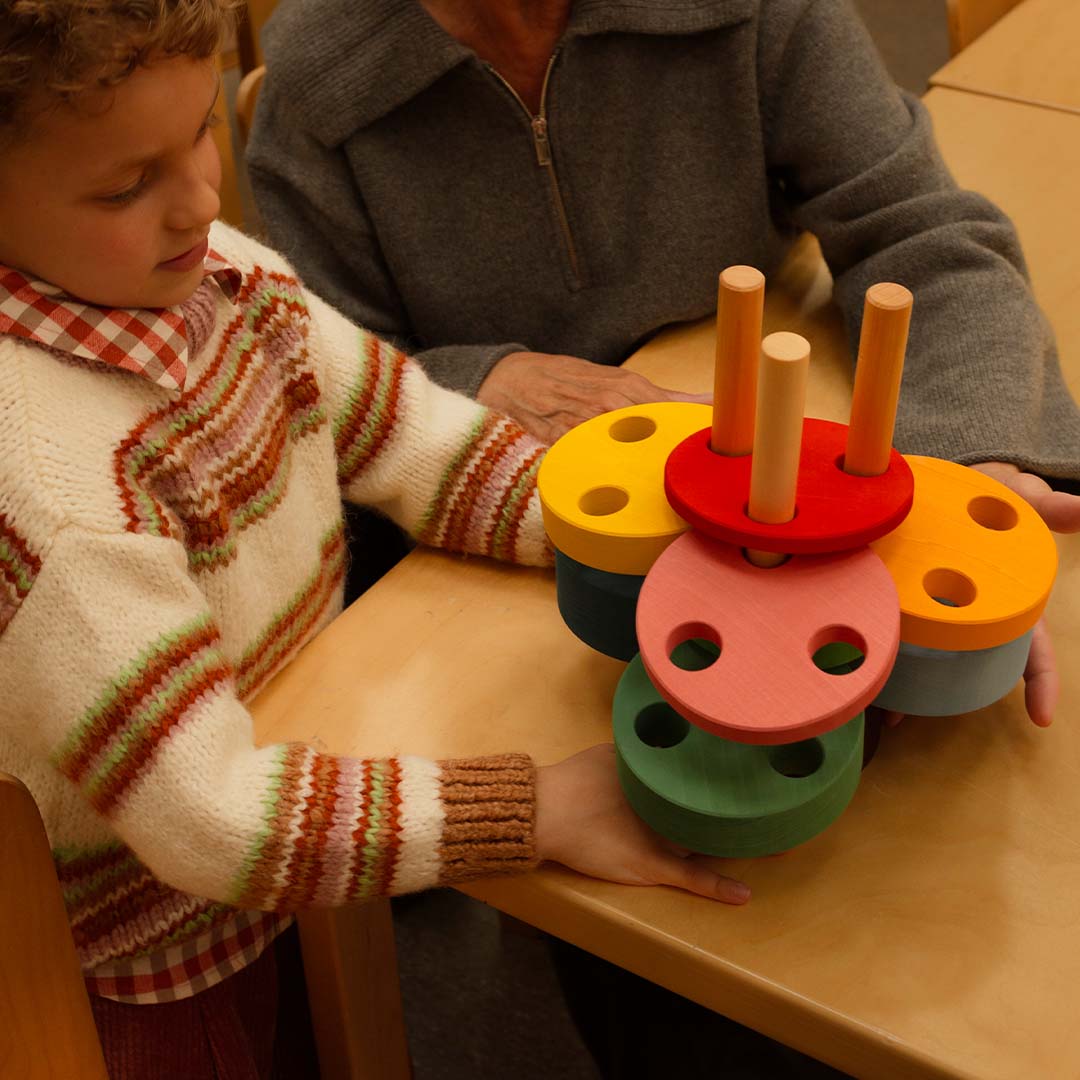 Een kind en een volwassene spelen samen met de toyto houten stapeltoren aan tafel.