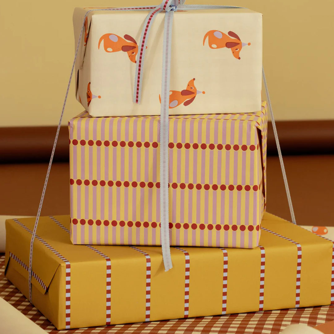 Drie gestapelde cadeaus, waarvan de onderste is ingepakt met ole inpakpapier met geel, rood en lichtblauw gestreept patroon.