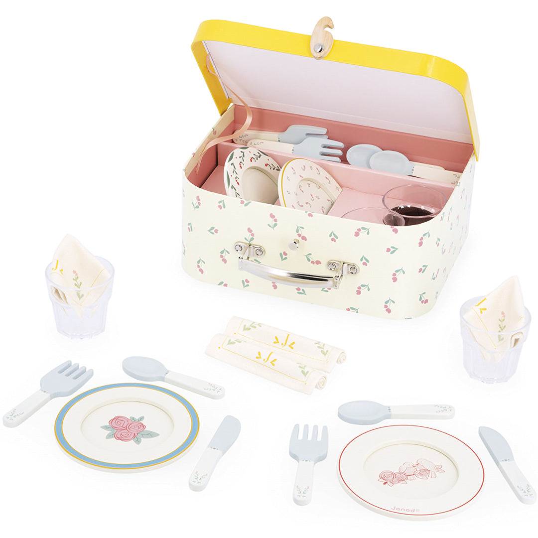 Janod speelgoed dinerset met gebloemd servies, bestek, glazen en servetten, deels in een open koffer.