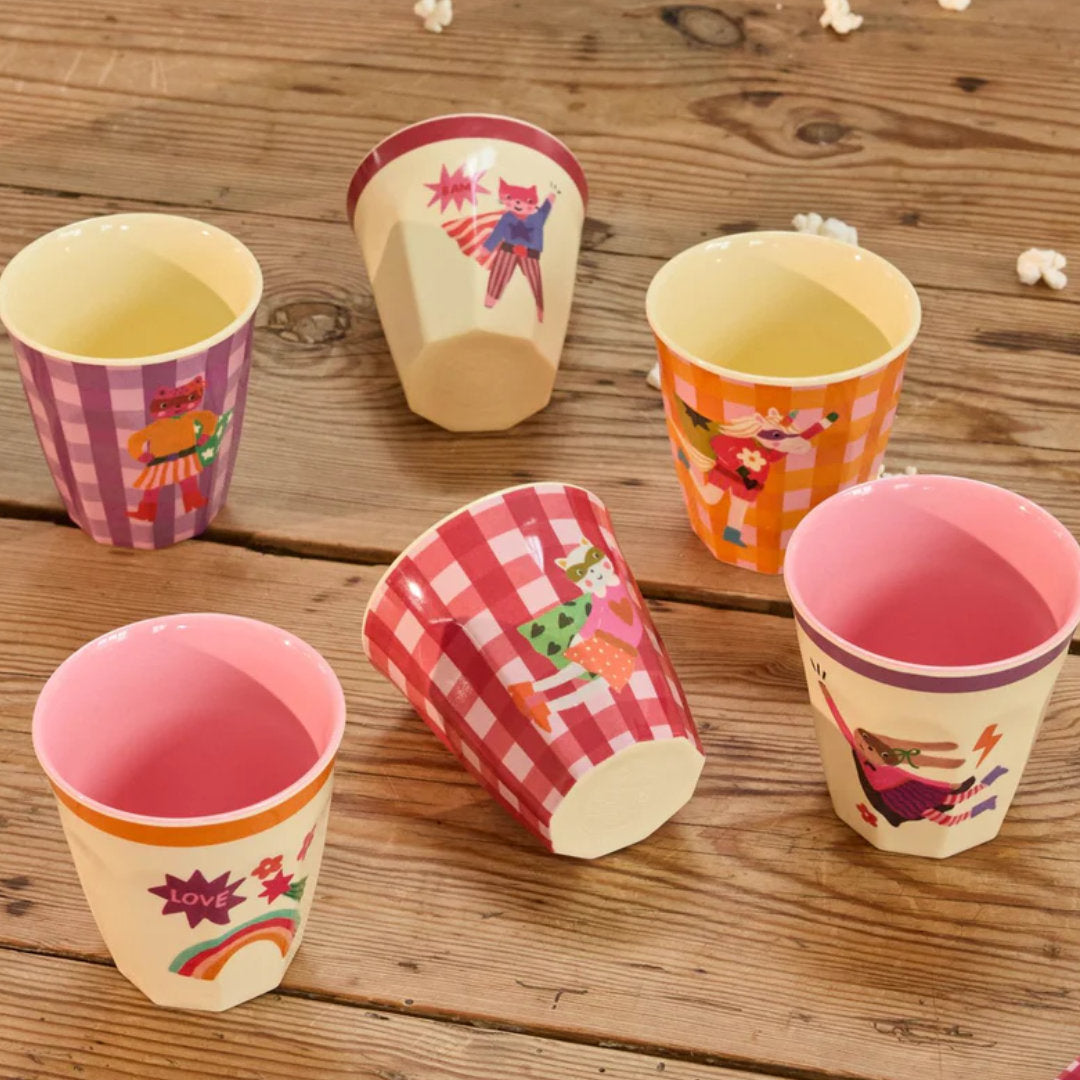 Zes Rice kinderbekers met superhelden dieren en geruite patronen verspreid op een houten tafel.