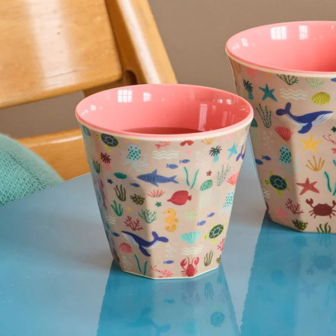 Twee rice kinderbekers met zeedierenpatroon op een blauwe tafel, waarvan één gevuld met een drankje.