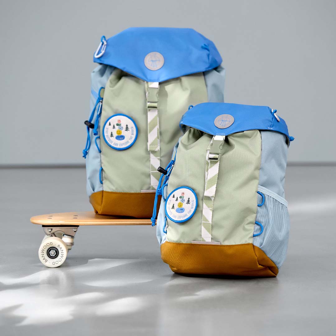 Twee Lässig kleuterrugzakken Sunny Explorer, een grote en een kleine, staan op een skateboard.