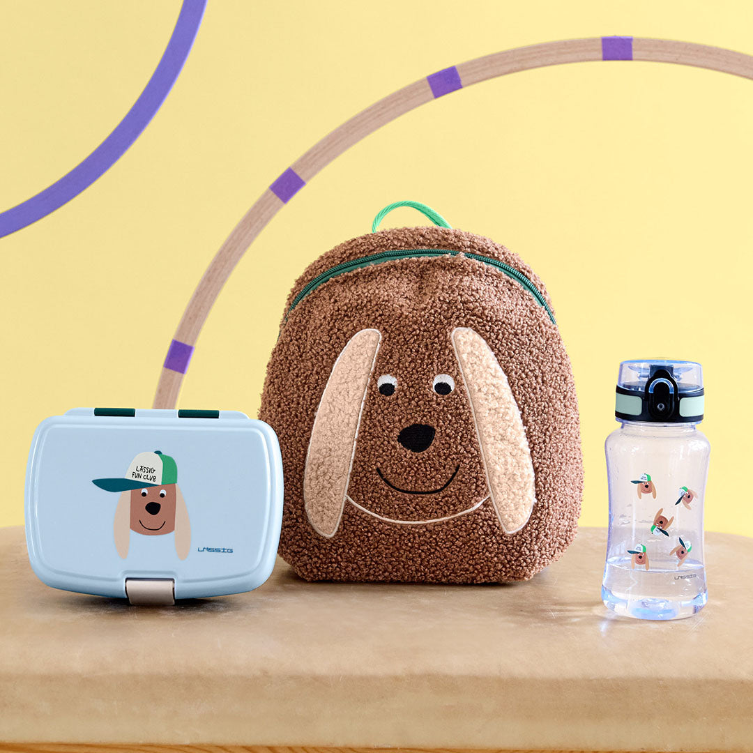 Lässig kinder drinkfles met hondenpatroon, lunchbox en rugzak in hondenthema op een houten ondergrond.
