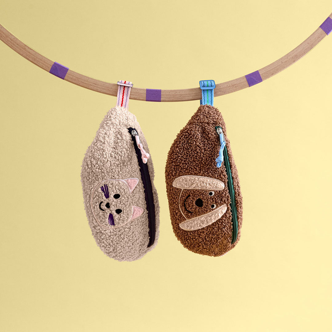 Twee kinder heuptassen, een beige kat en een bruine aap, hangen aan een houten stang.