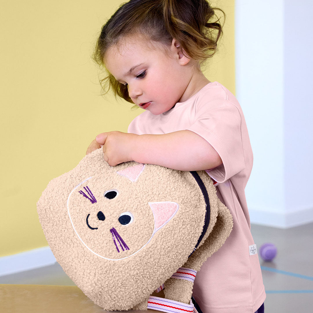 Een peuter houdt de Lässig beige kattenrugzak vast.