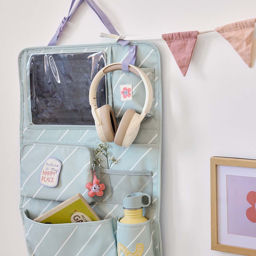 Lässig auto organizer voor kinderzitjes, groen met witte strepen, hangend aan een muur en gevuld met een tablet, koptelefoon en andere spullen.