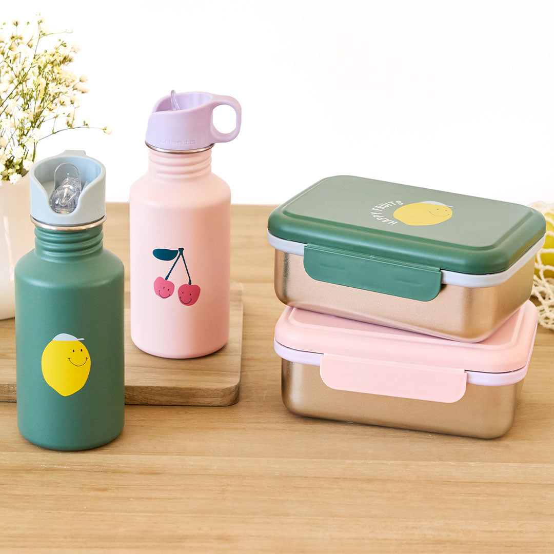 Lässig collectie van twee kinder drinkflessen en twee lunchboxen met kersen- en citroenprints op een houten tafel.