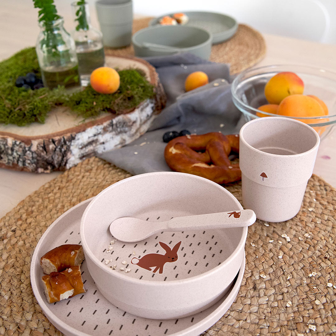 De lässig beige babyserviesset met konijnenthema staat op een tafel met fruit en snacks.