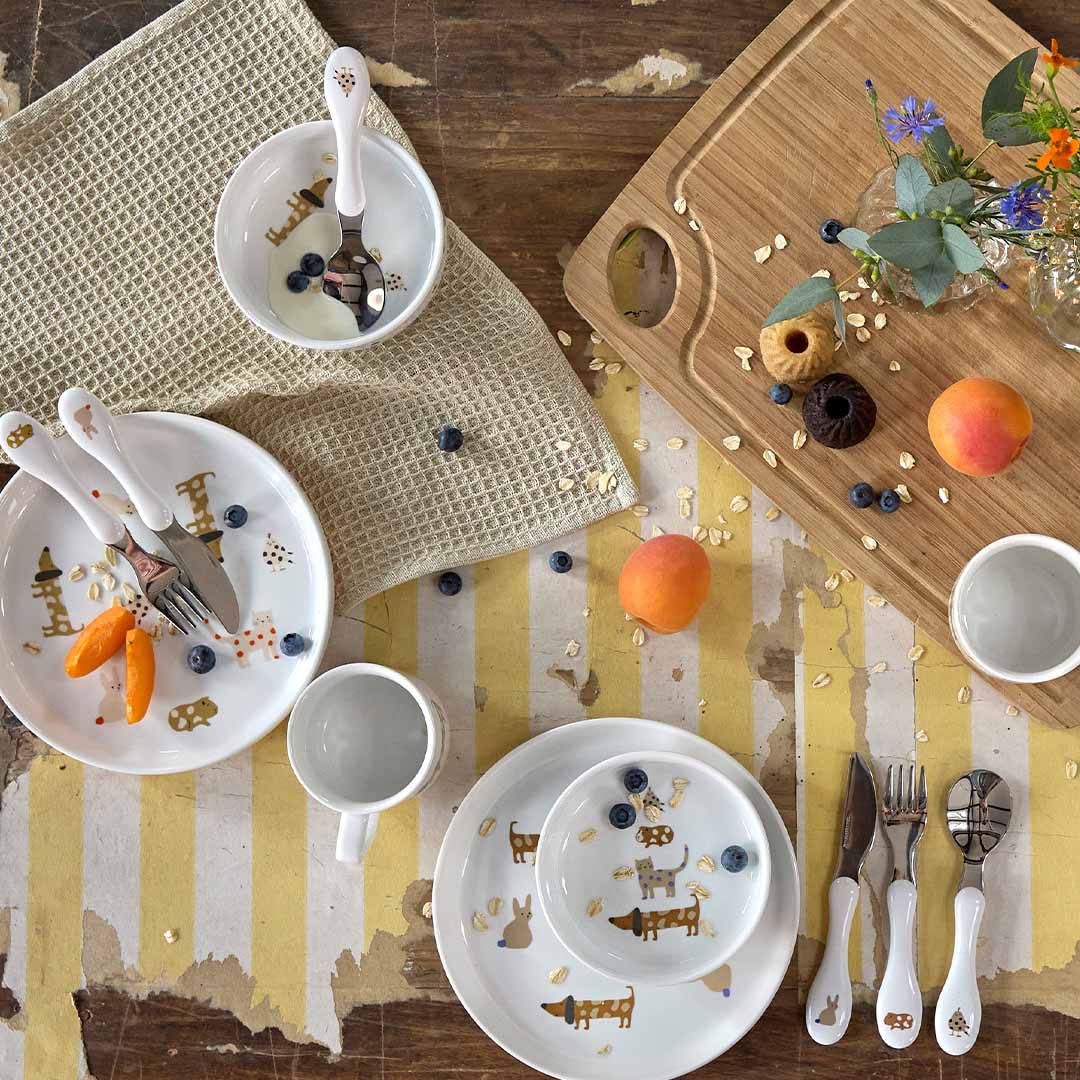 Een tafel vol lässig kinderbestek en servies met dierenpatronen, samen met fruit en snacks.
