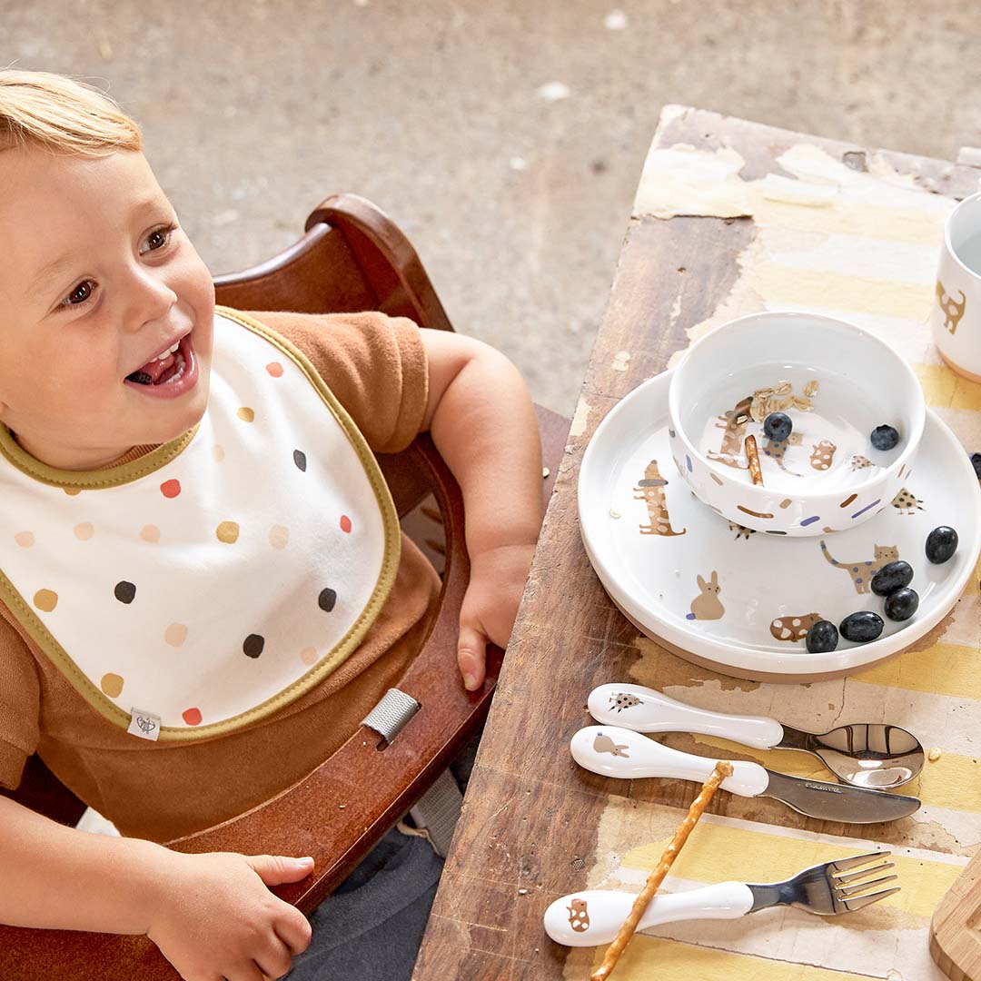 Een lachende peuter in een kinderstoel met de Lässig porseleinen serviesset met dierenpatroon en blauwe bessen op tafel.