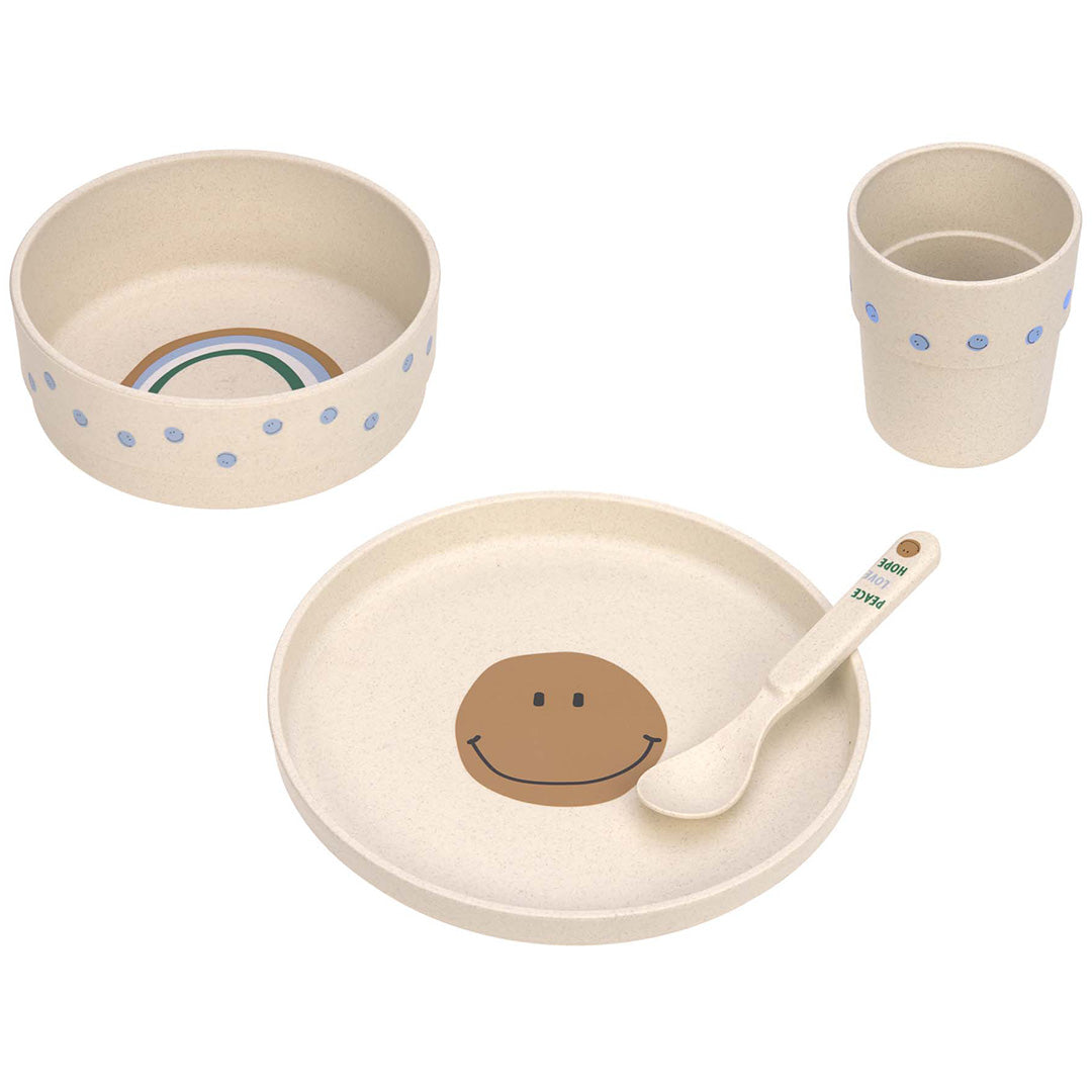 lässig babyserviesset met beige kom met regenboog, bord met bruine smiley, beker met blauwe stippen en lepel met tekst.