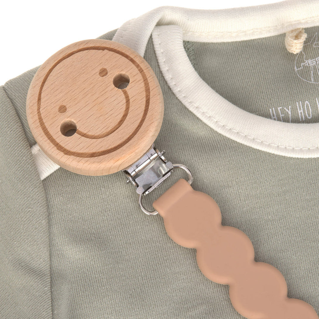 Lässig speenkoord met houten smiley clip bevestigd aan een groen babyrompertje.