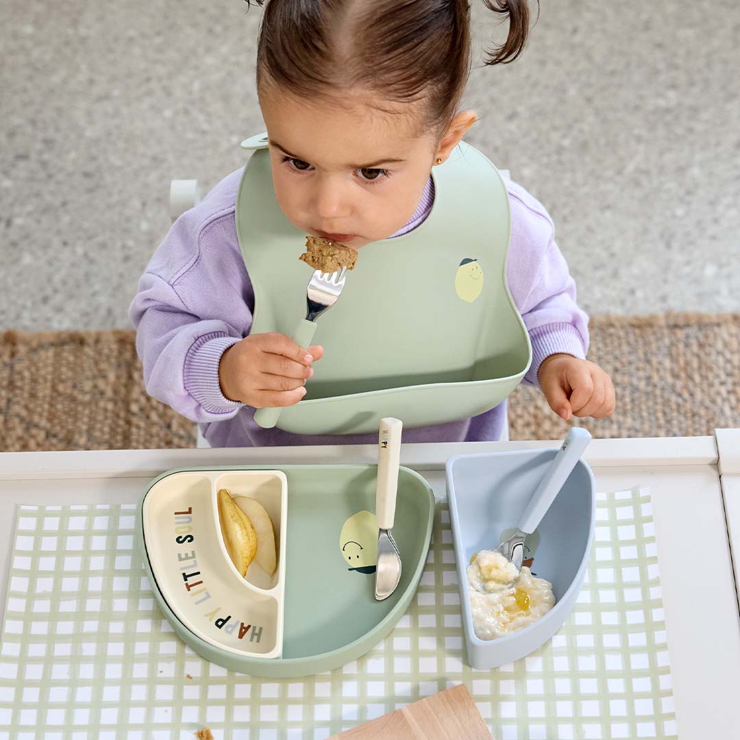 Een peuter in een kinderstoel eet met het Lässig kinderbestek van een bord met citroenthema.