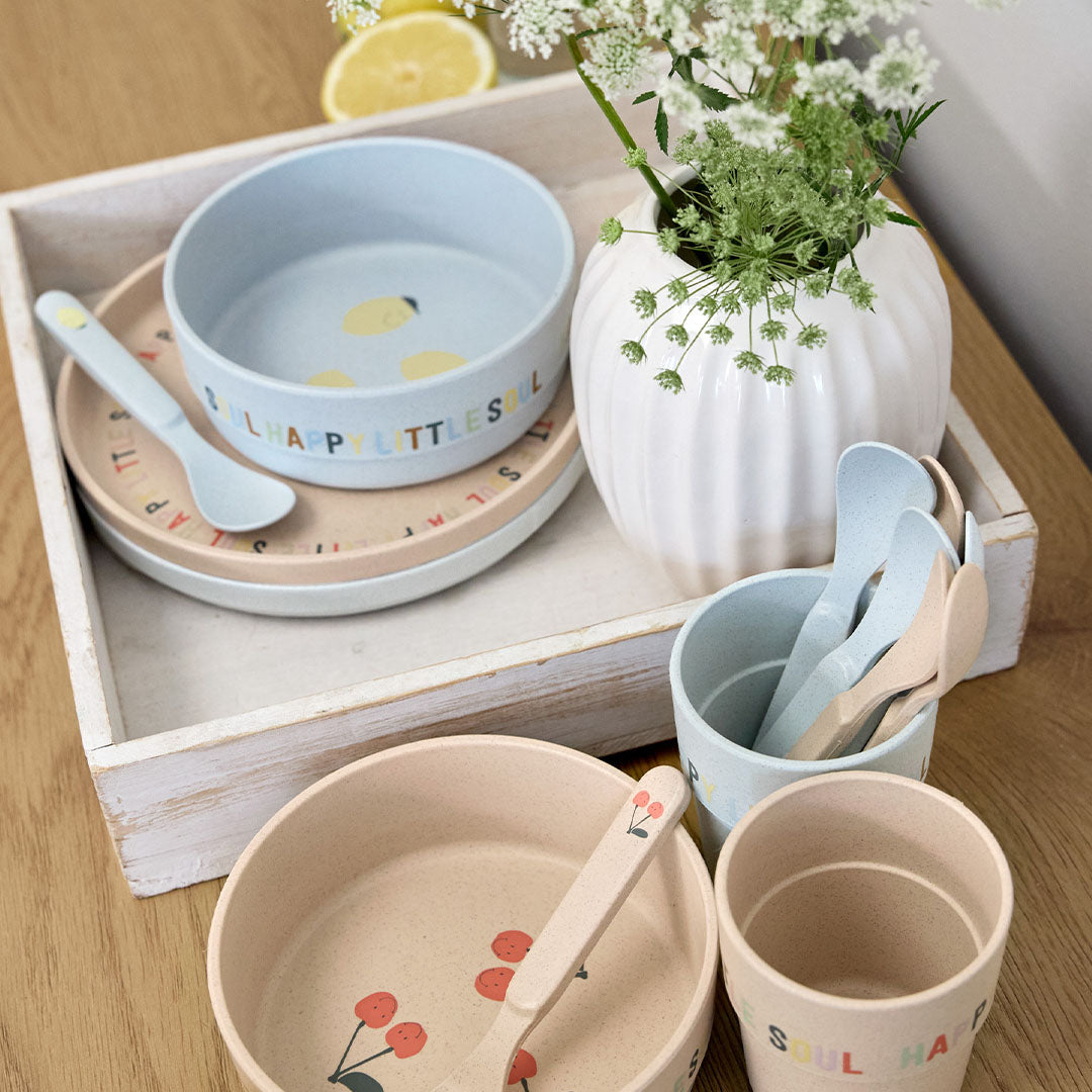Een collectie van Lässig baby serviessets in lichtblauw met citroenprint en beige met kersenprint op een dienblad.