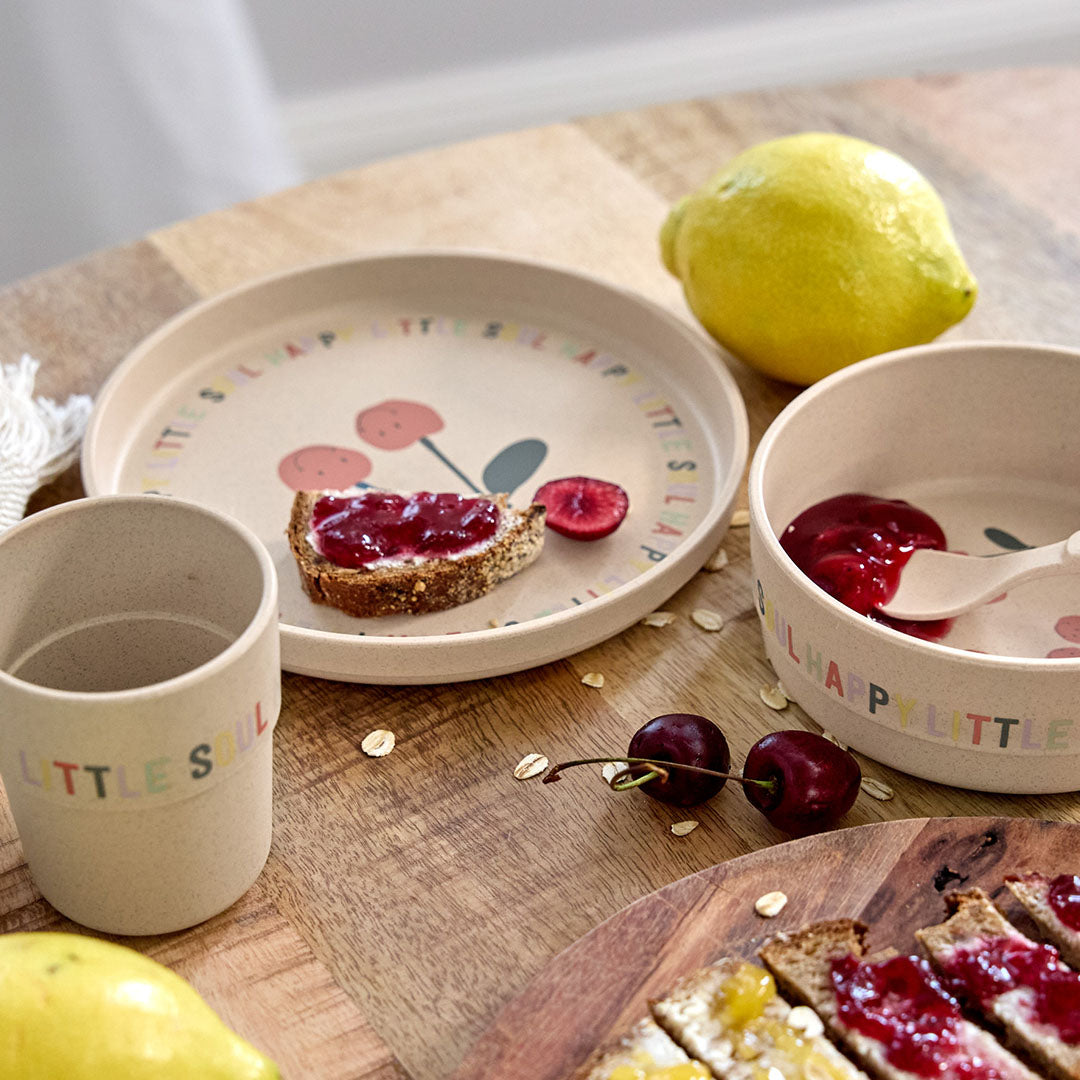 De Lässig beige serviesset voor baby's en peuters met kersenpatroon staat op een houten tafel met een belegd broodje en fruit.