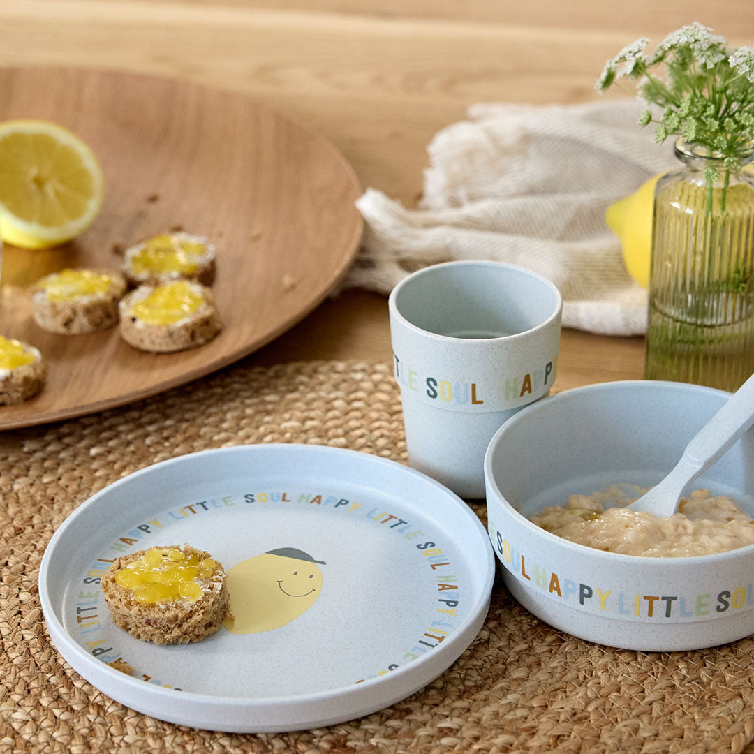 De Lässig lichtblauwe baby serviesset met citroenprint staat op een tafel met ontbijt en een halve citroen.