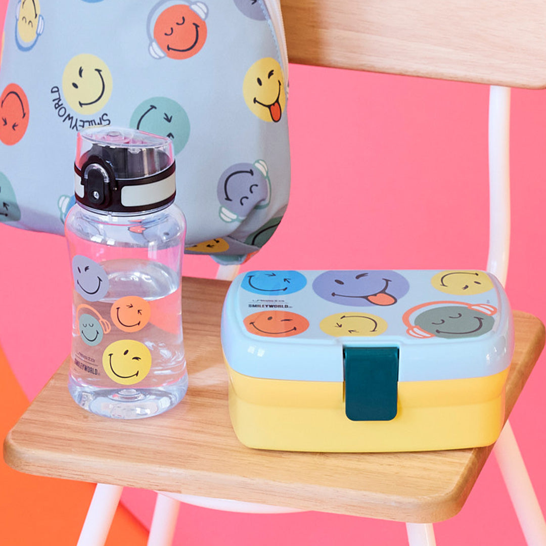 De Lässig Smileyworld kinderdrinkfles staat naast een bijpassende lunchbox op een houten stoel.