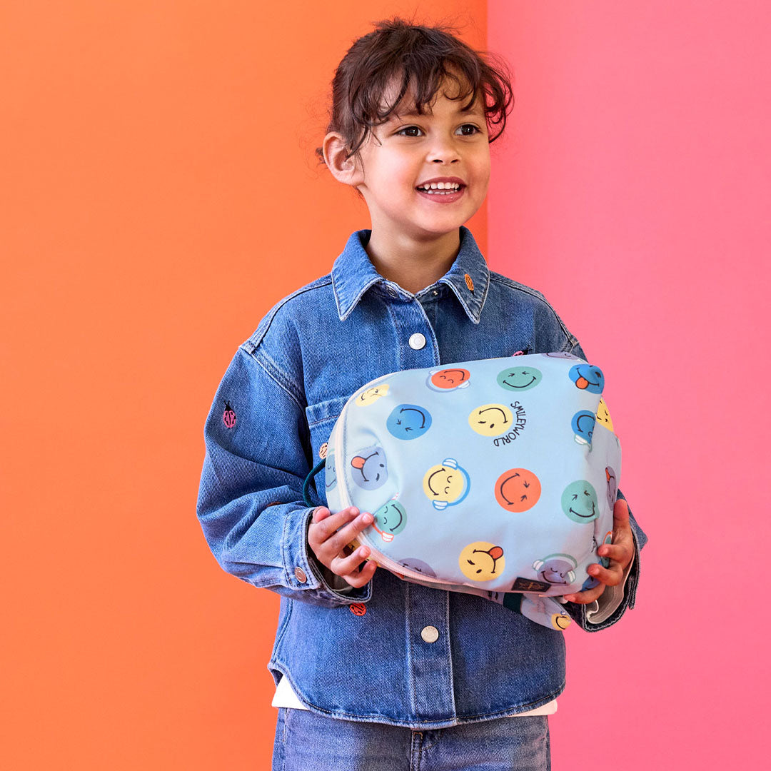 Een kind houdt de blauwe peuterrugzak met smileyworld-print tegen de borst.