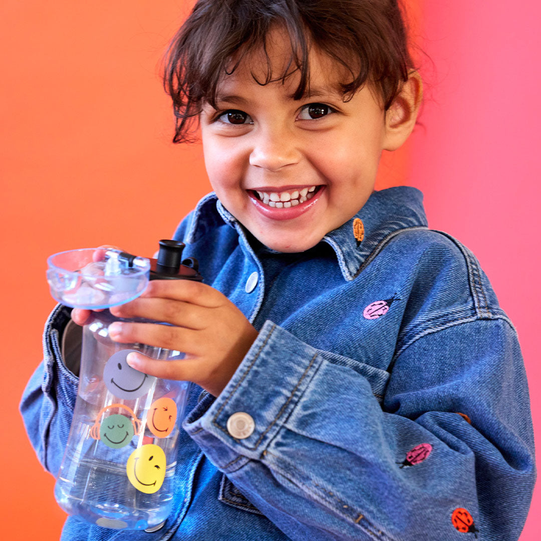 Een lachend kind houdt de Lässig Smileyworld kinderdrinkfles met water vast.