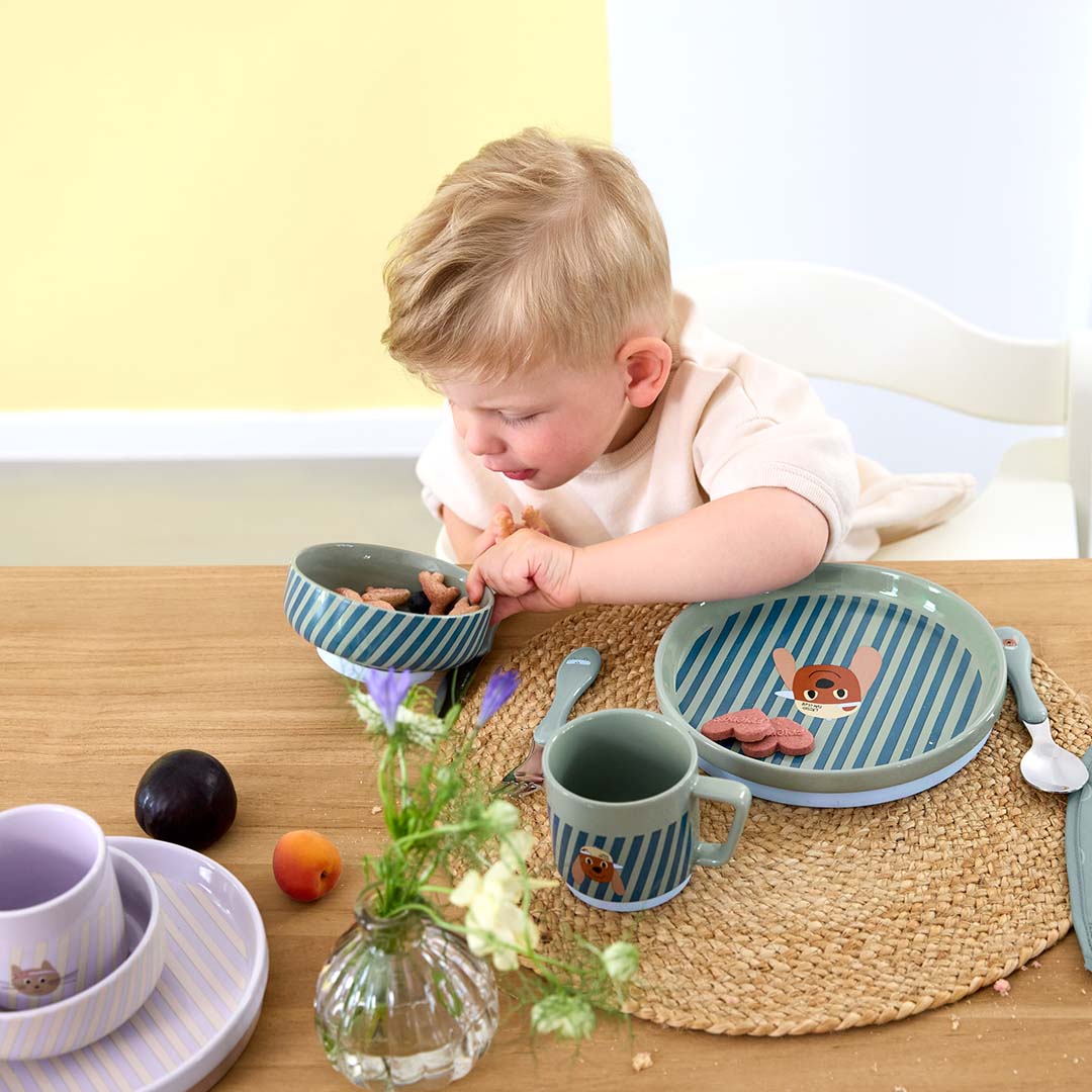 Een kindje kijkt geconcentreerd naar de Lässig porseleinen serviesset met hondenfiguur op een houten tafel.