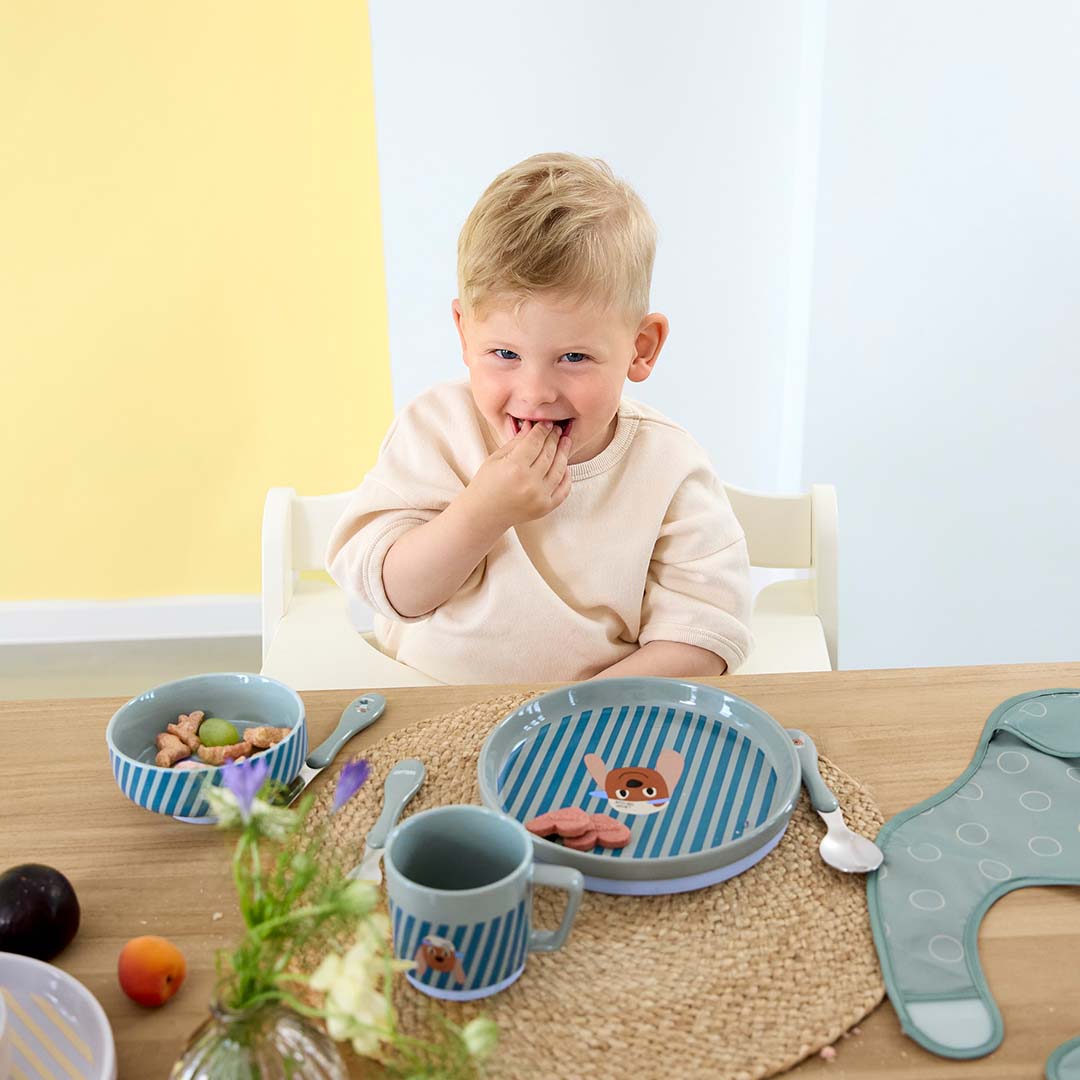 Een lachend kindje eet aan tafel met de Lässig porseleinen serviesset met hondenfiguur.
