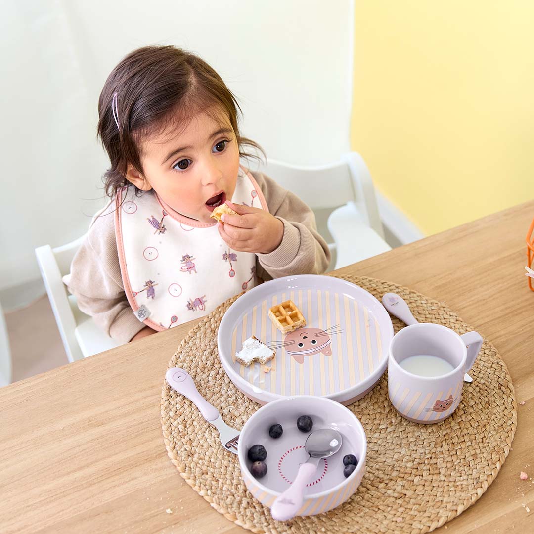 Een kind eet aan tafel met de Lässig kinder serviesset met kattengezicht en paarse strepen.