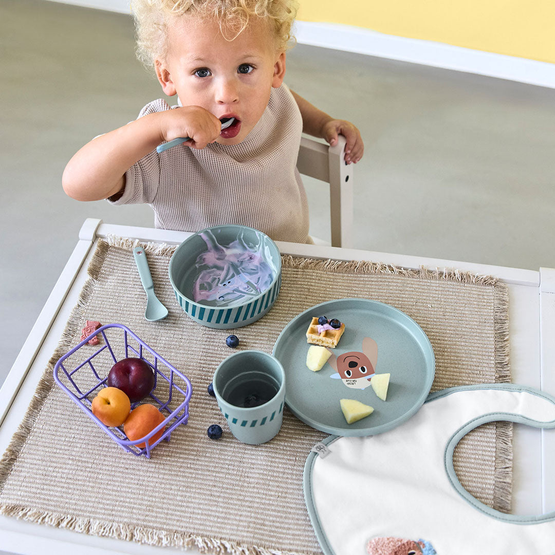 Een peuter eet met een lepel uit de groene lässig babyserviesset met hondenfiguur.