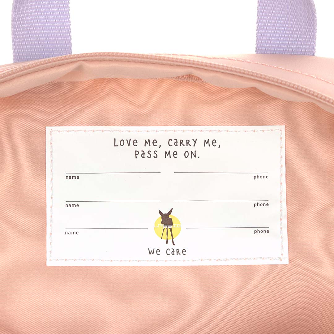 Een close-up van het interne label in de Lässig kleuterrugzak met de tekst 'Love Me, Carry Me, Pass Me On' en ruimte voor namen.