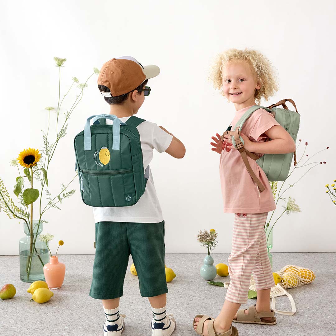 Twee kinderen dragen Lässig kleuterrugzakken, de jongen een donkergroene met citroen en het meisje een lichtgroene.