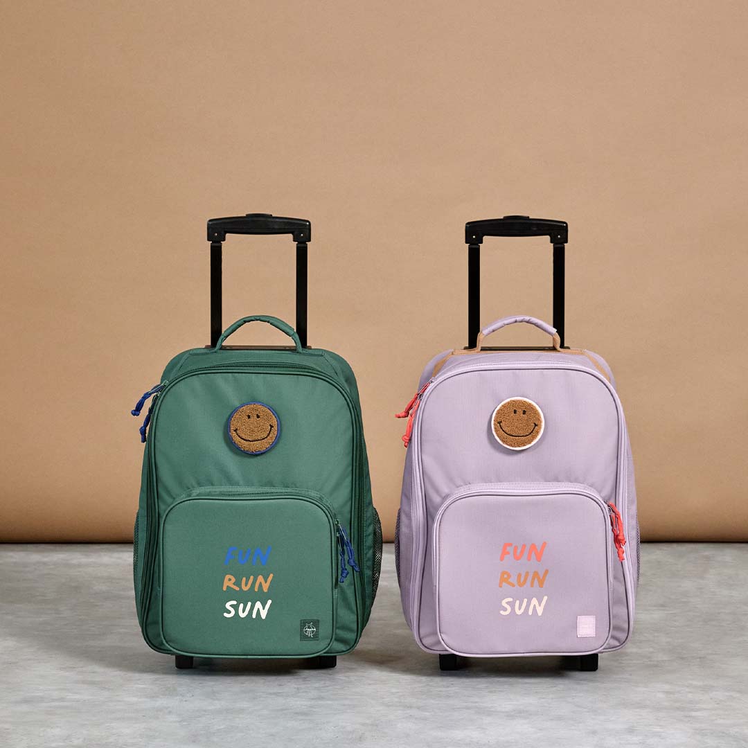 Twee lässig kinderkoffers, een groene en een lila, met smiley patch en de tekst 'FUN RUN SUN'.