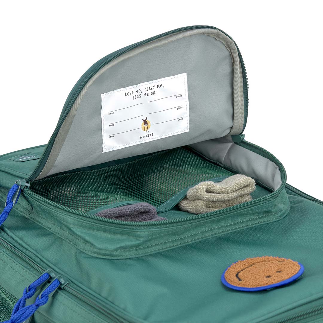 De lässig kinderkoffer geopend, met een mesh vak, kleding en een label met de tekst 'Love me, carry me, pass me on'.