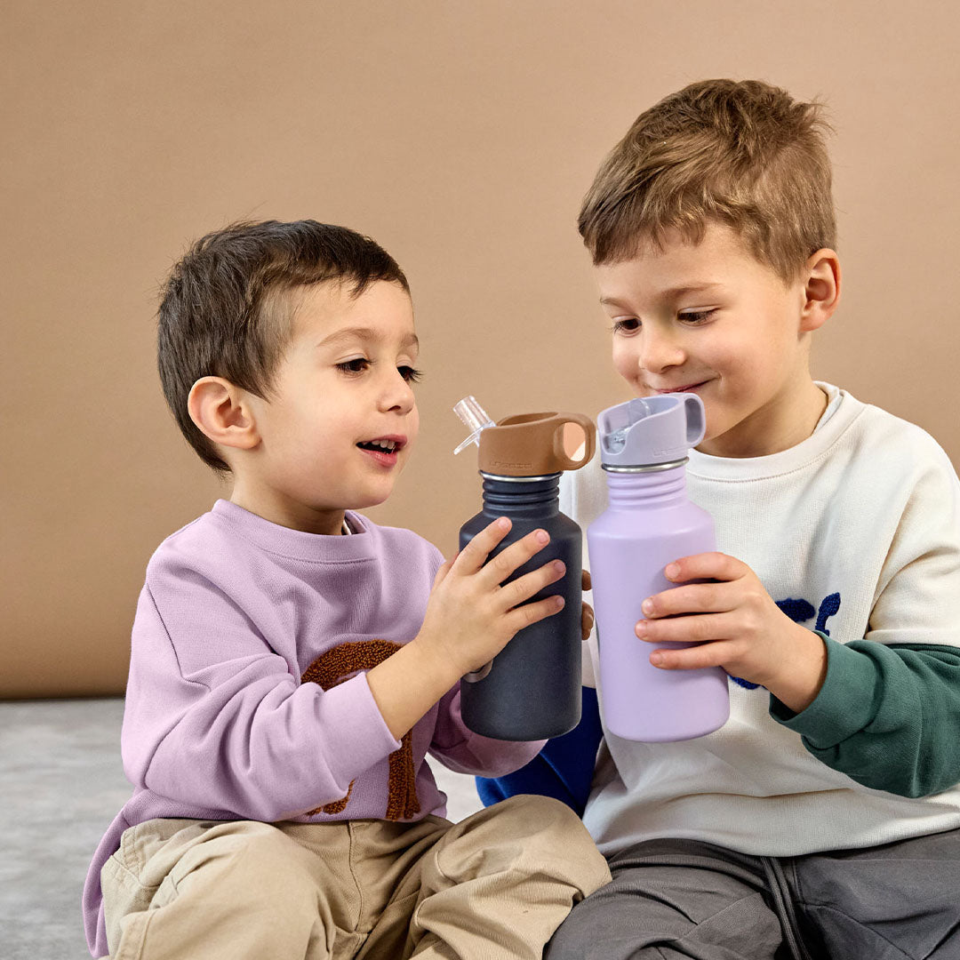 Twee jongetjes houden elk een Lässig kinder drinkfles vast, één marineblauw met smile en één lila.
