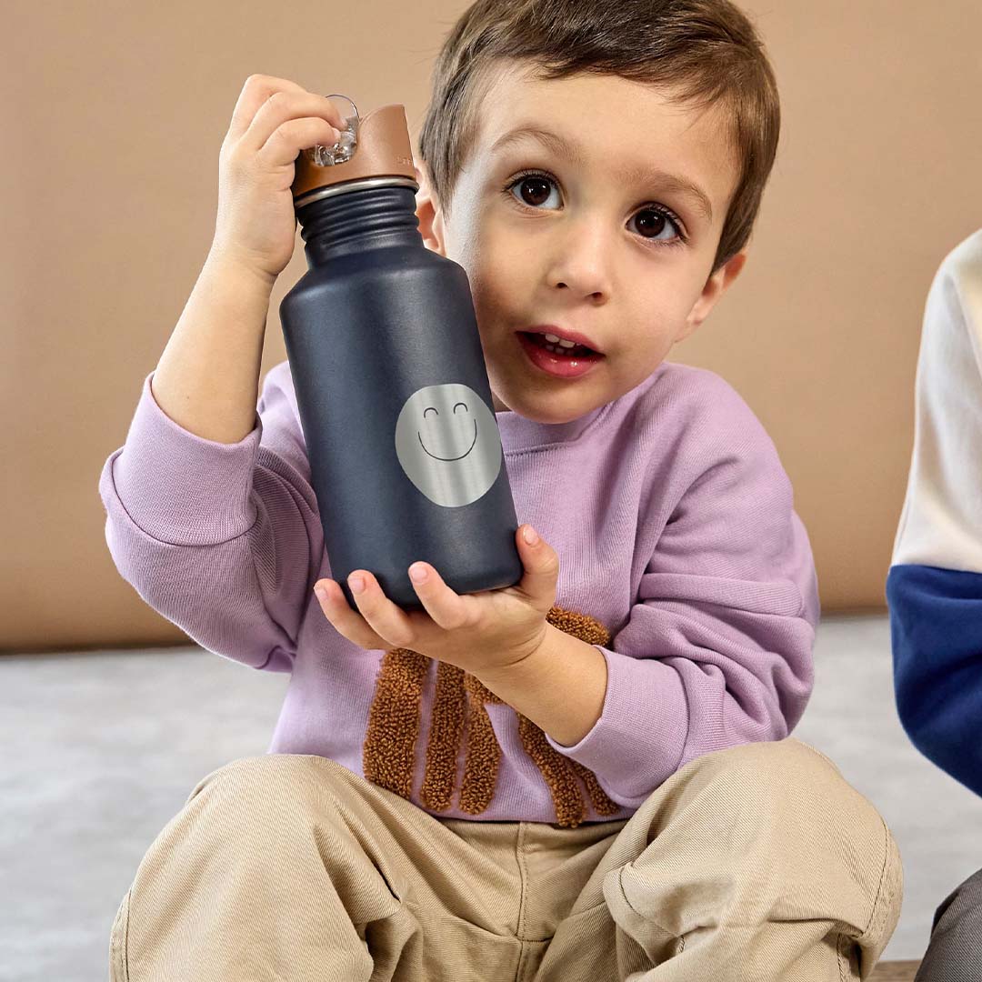 Een jongetje houdt de Lässig marineblauwe kinder drinkfles met smile-gezicht vast.