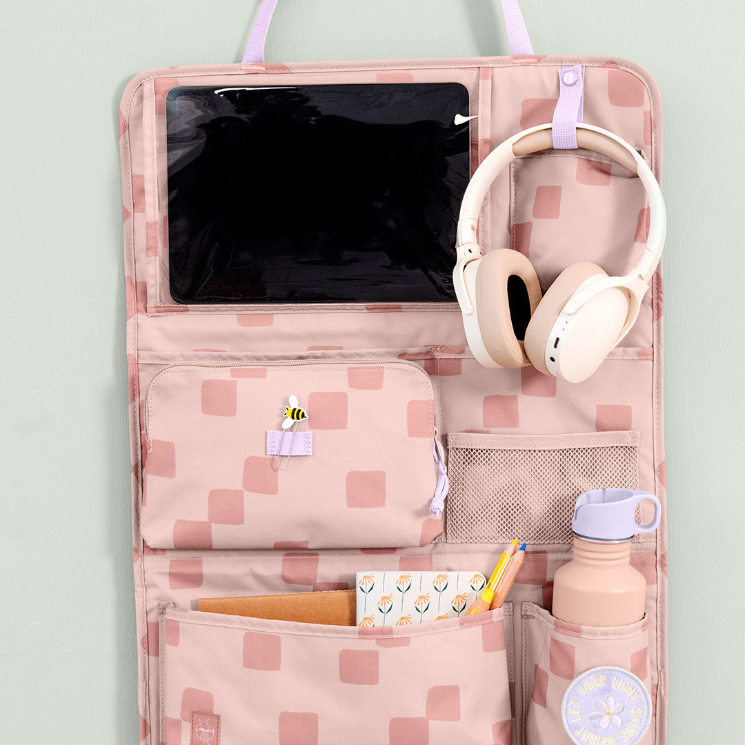 Lässig roze geruite auto organizer met een tablet, koptelefoon, waterfles en schrijfwaren.