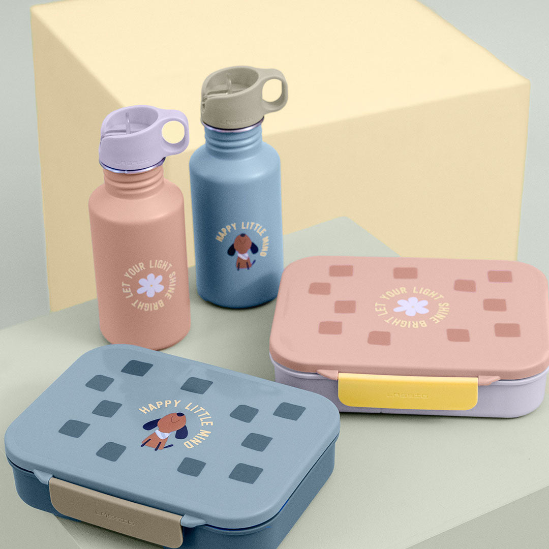 Twee Lässig kinder drinkflessen en twee bijpassende lunchboxen met hondje en tekst op een lichte achtergrond.