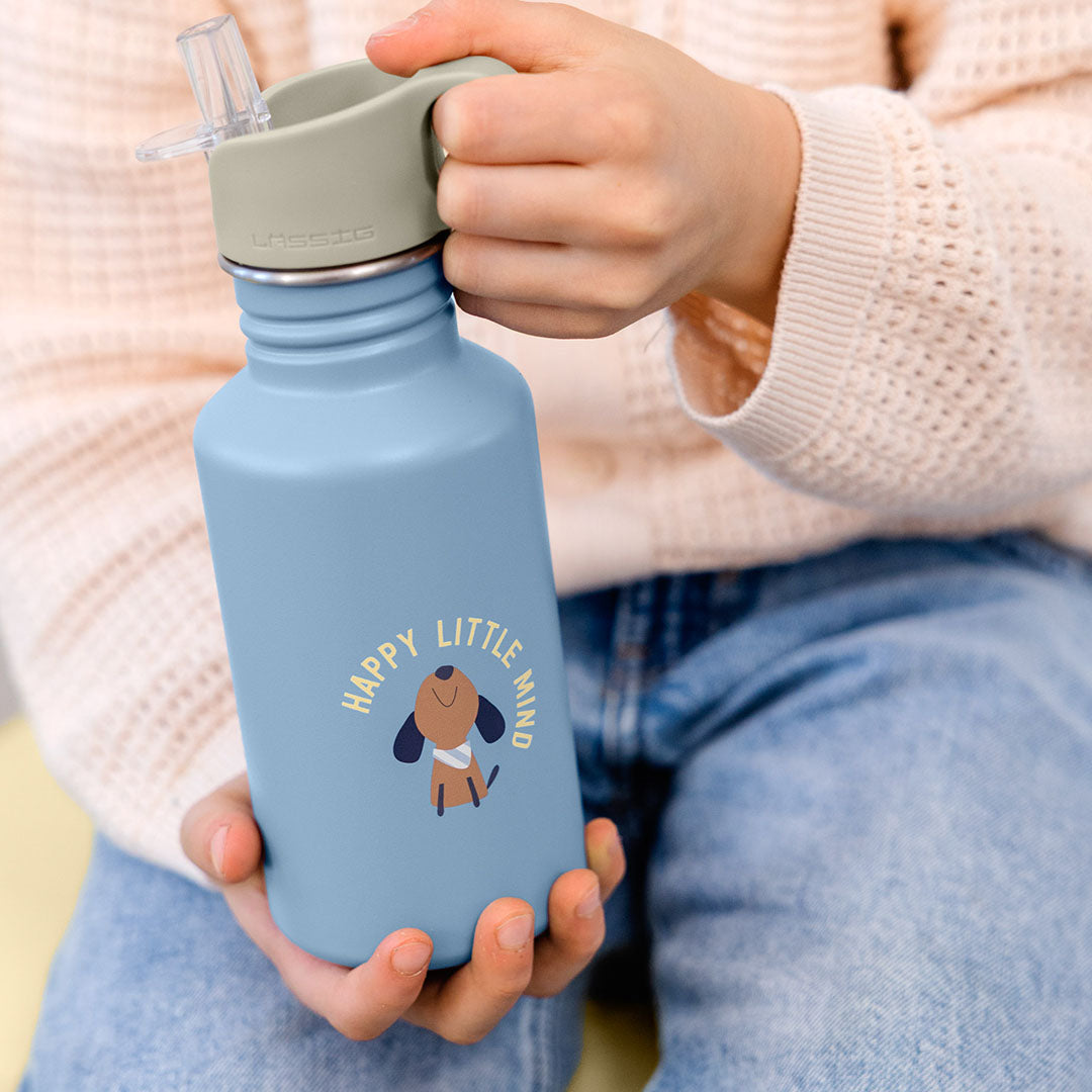 Een kind houdt de lichtblauwe Lässig kinder drinkfles met hondje en tekst vast.