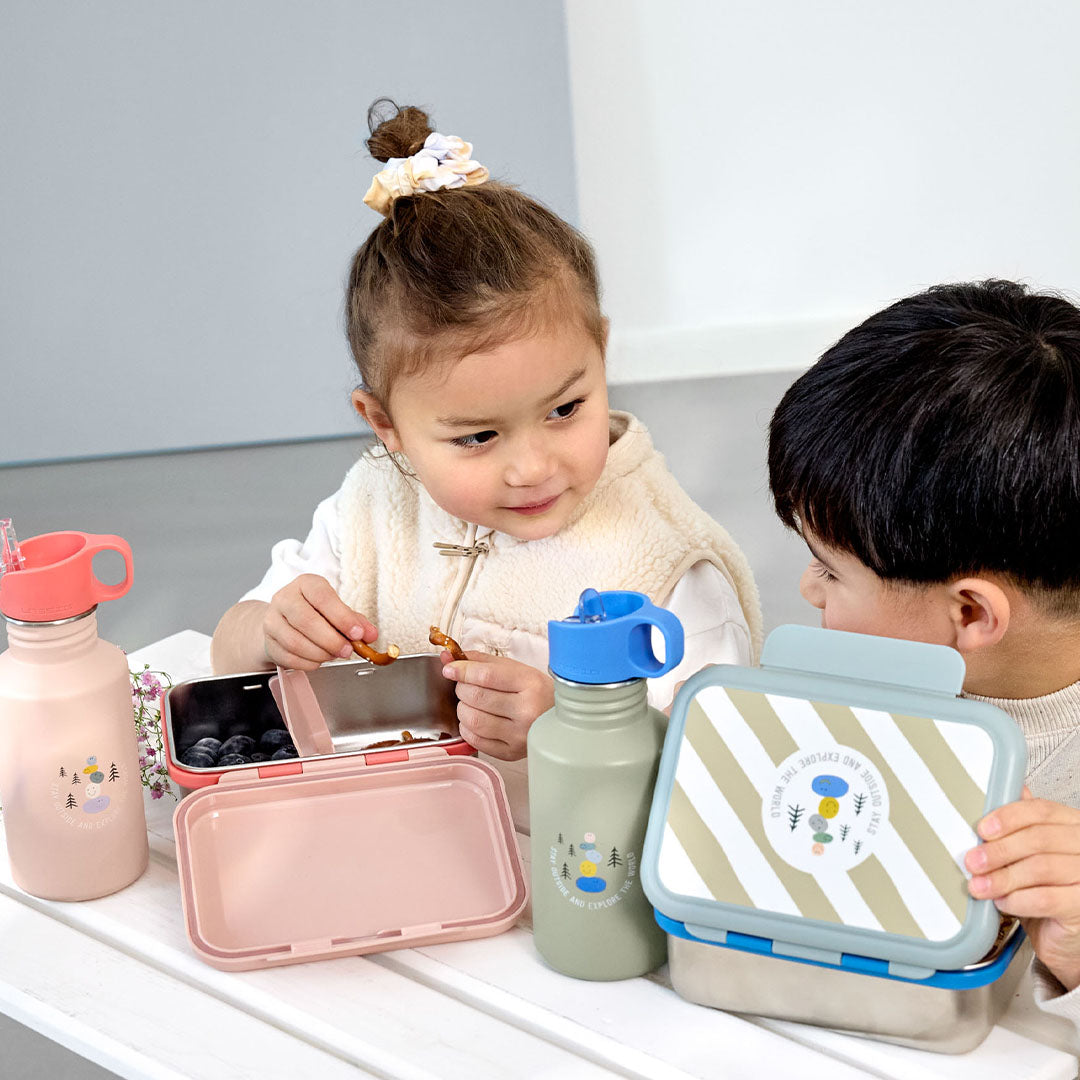 Twee kinderen zitten aan tafel met Lässig kinder drinkflessen en bijpassende lunchboxen.