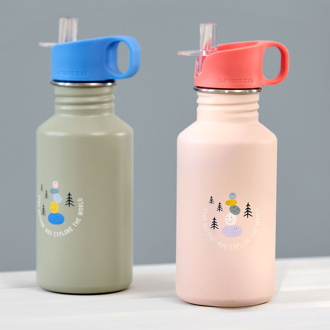 Twee Lässig roestvrijstalen kinder drinkflessen, één roze en één groen, met een opdruk van vrolijke stenen en bomen.