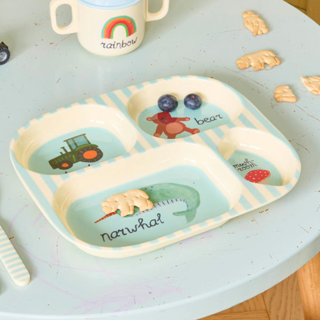 rice vakjesbord met blauwe strepen en afbeeldingen van een tractor, beer, narwal en paddenstoel, met daarin fruit en een koekje.