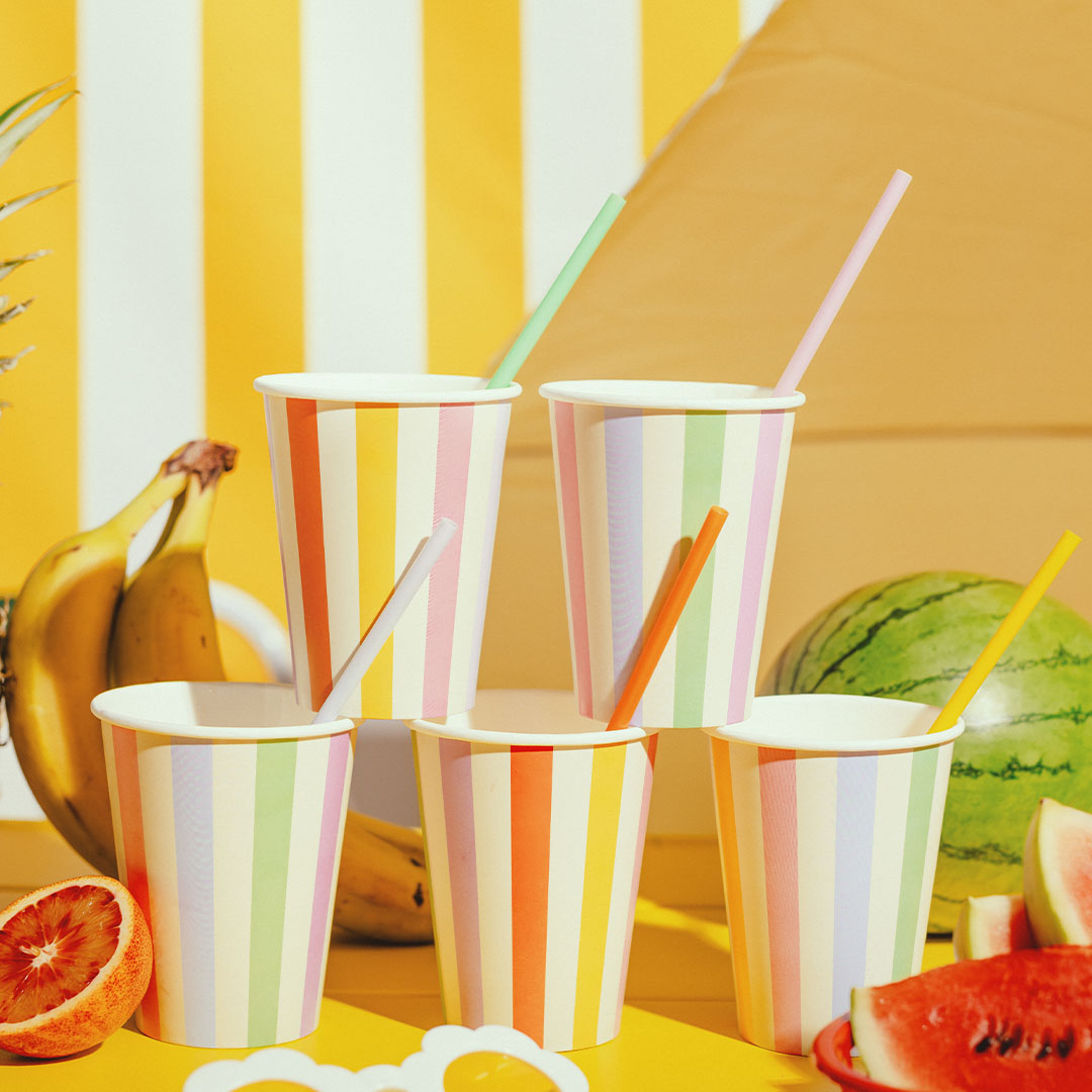 Partydeco gestreepte papieren feestbekers met rietjes in een zomerse setting met fruit.
