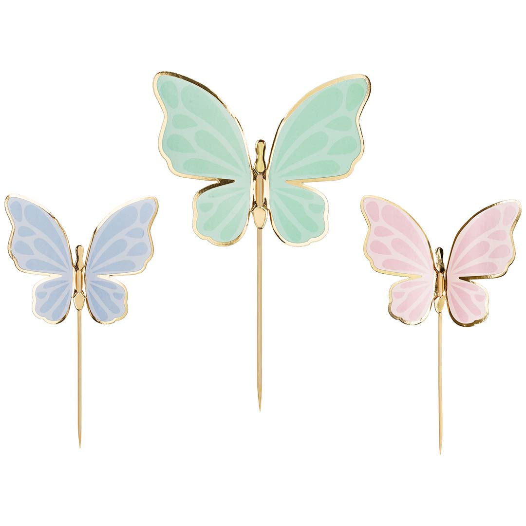 Drie partydeco vlinder taarttoppers in pastelkleuren met gouden randen op een witte achtergrond.