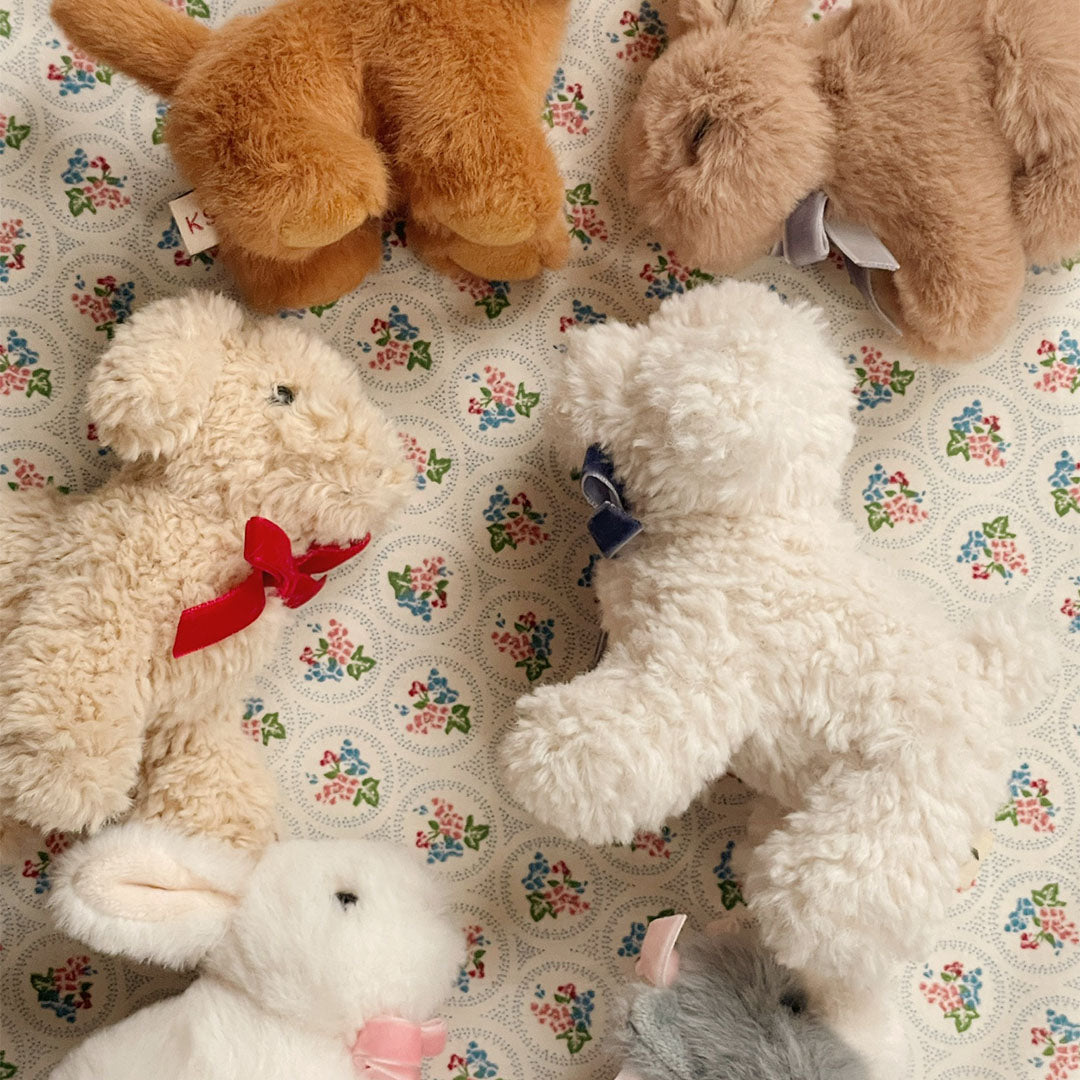 Een collectie van Konges Sløjd pluchen knuffeldieren, waaronder honden, een konijn en een kat, op een bloemige ondergrond.