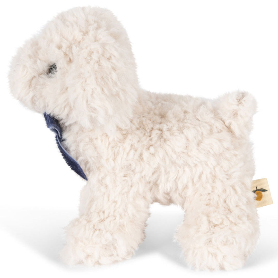 Konges Sløjd witte pluchen knuffelhond met blauwe strik, van de linkerzijkant gefotografeerd.