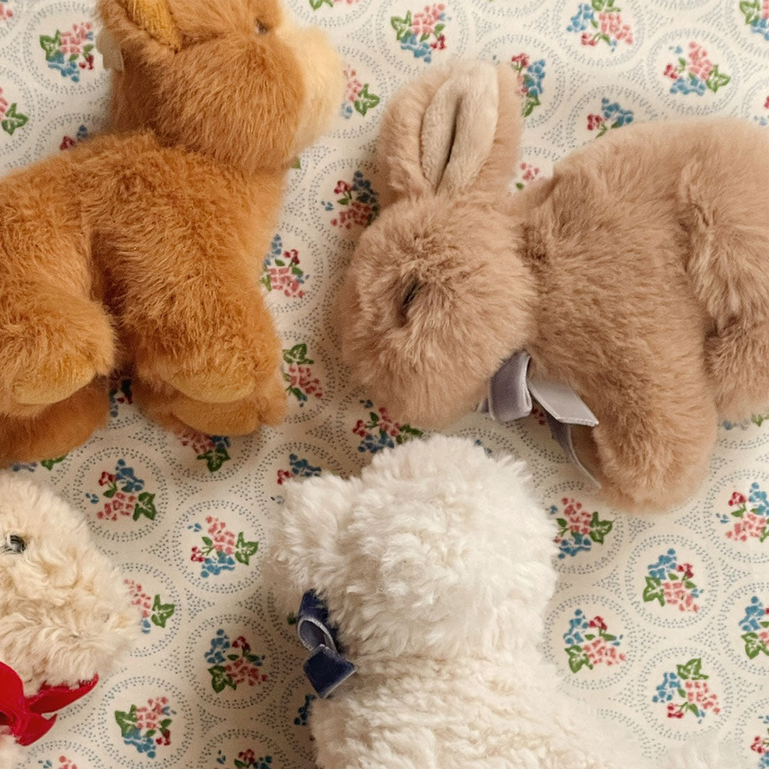 Een Konges Sløjd pluchen knuffelkonijn en andere knuffels liggen op een stof met bloemenpatroon.