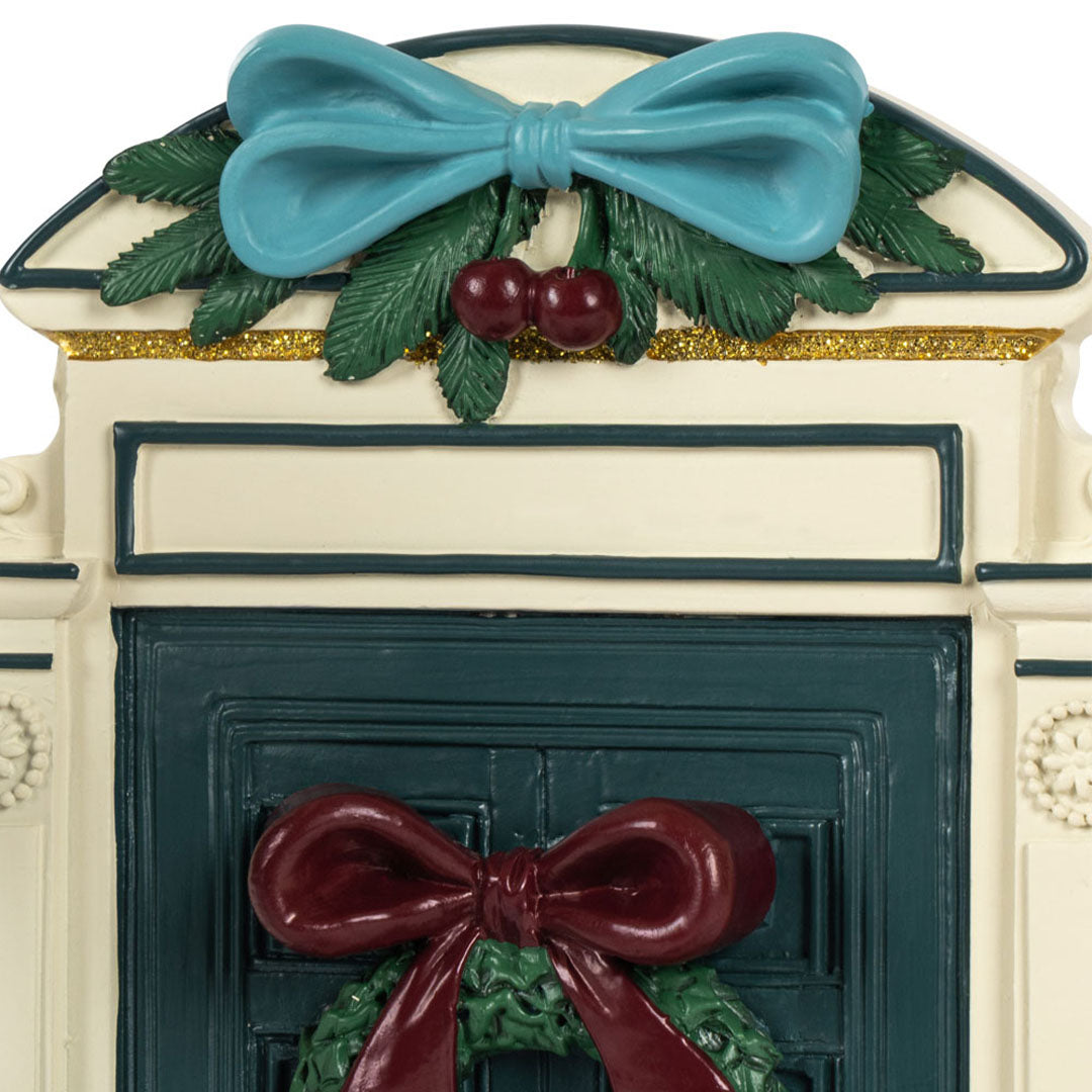 Detail van de bovenkant van de miniatuur kerstdeur met blauwe strik en kerstversiering.