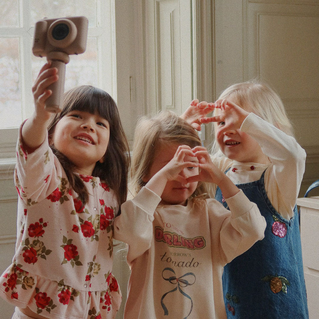 Drie lachende kinderen spelen met de kindercamera, waarvan één kind de camera omhoog houdt.
